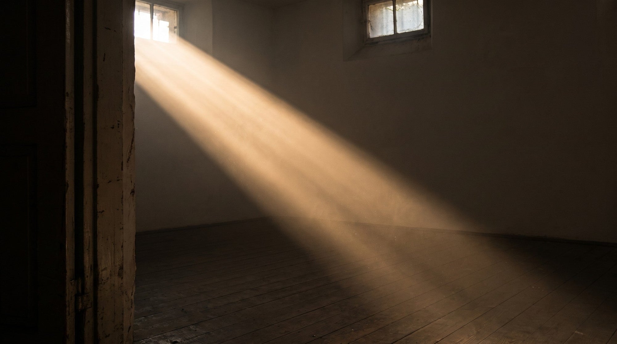 A shaft of warm low sunlight crossing a dim, empty room, making the dust and air visible.