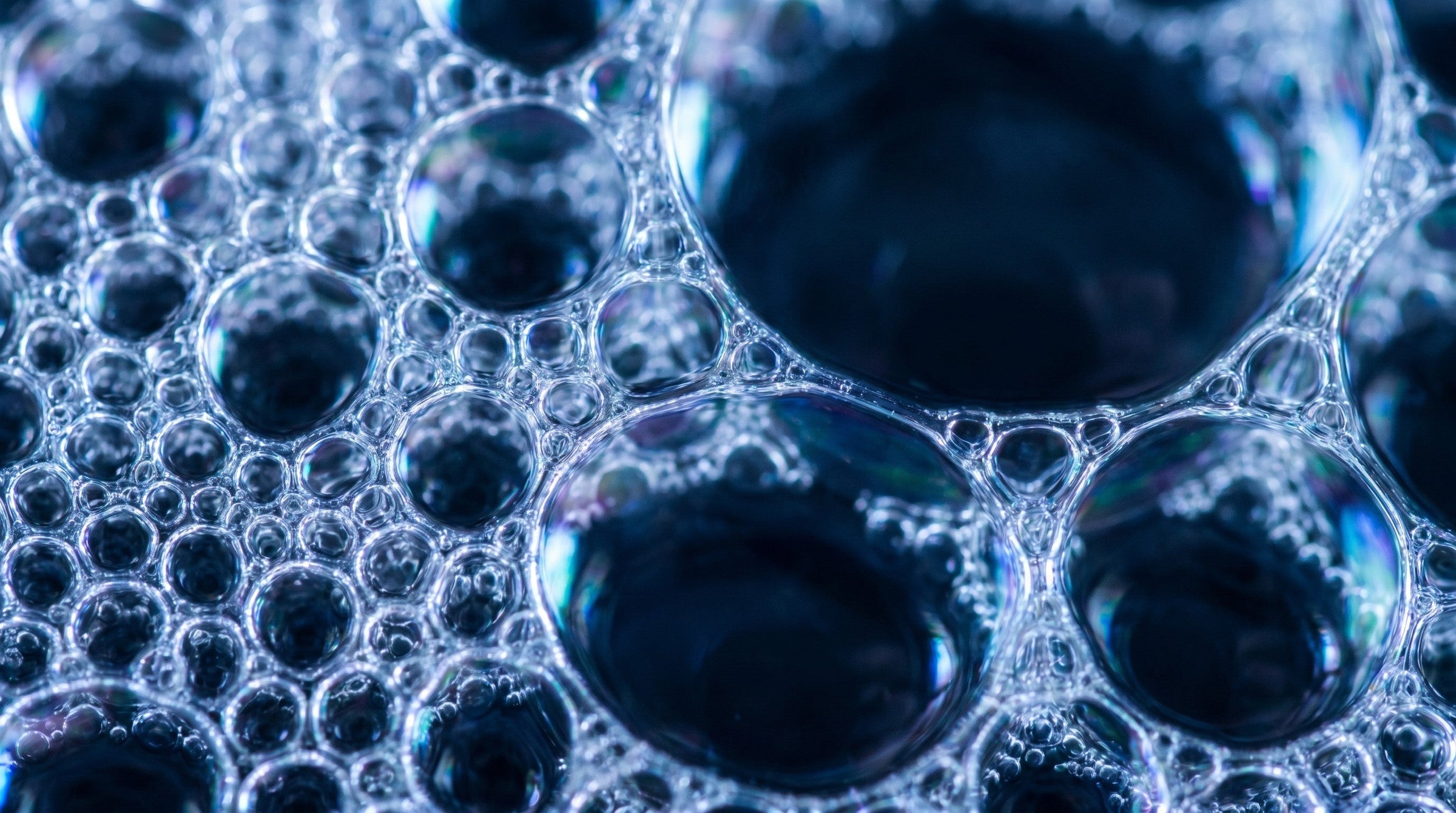 Macro of dense soap lather bubbles catching cool light against a dark background.