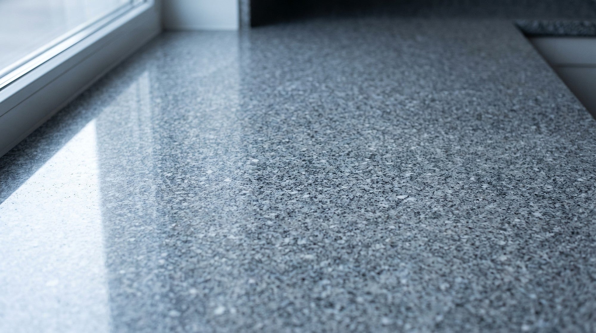 Low daylight raking across a polished speckled granite countertop, showing the stone's grain and sheen.