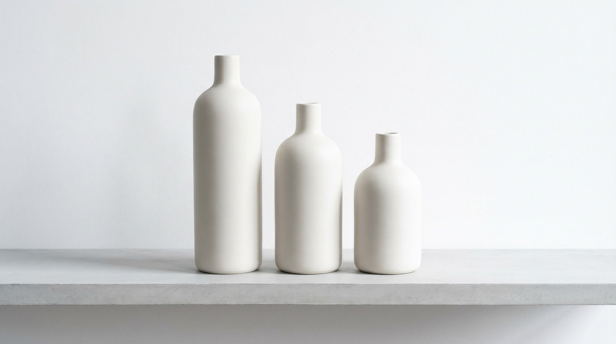 Several plain unlabeled bottles turned backwards on a pale grey surface, their blank backs to the camera.