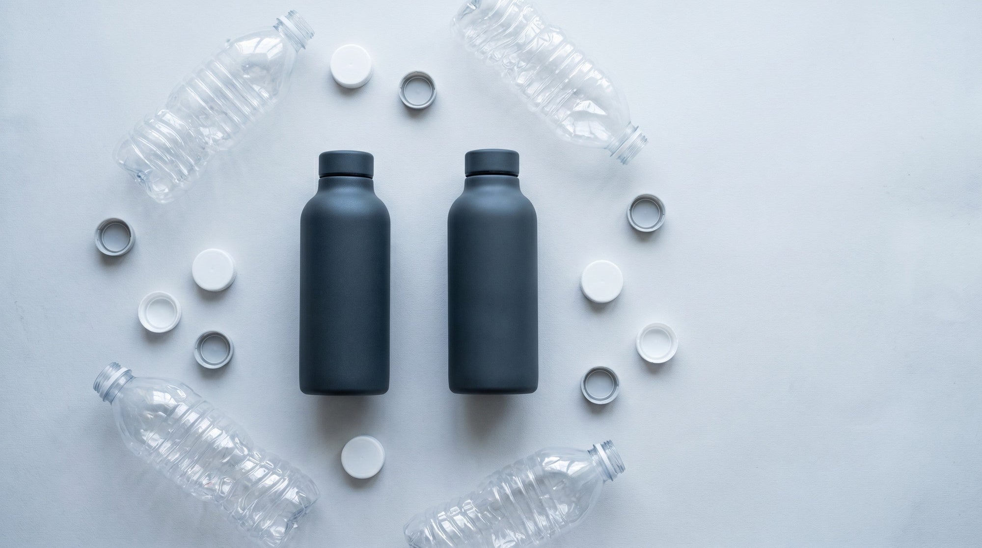 Overhead view of one sturdy refillable bottle surrounded by small empty plastic bottles on a muted surface.