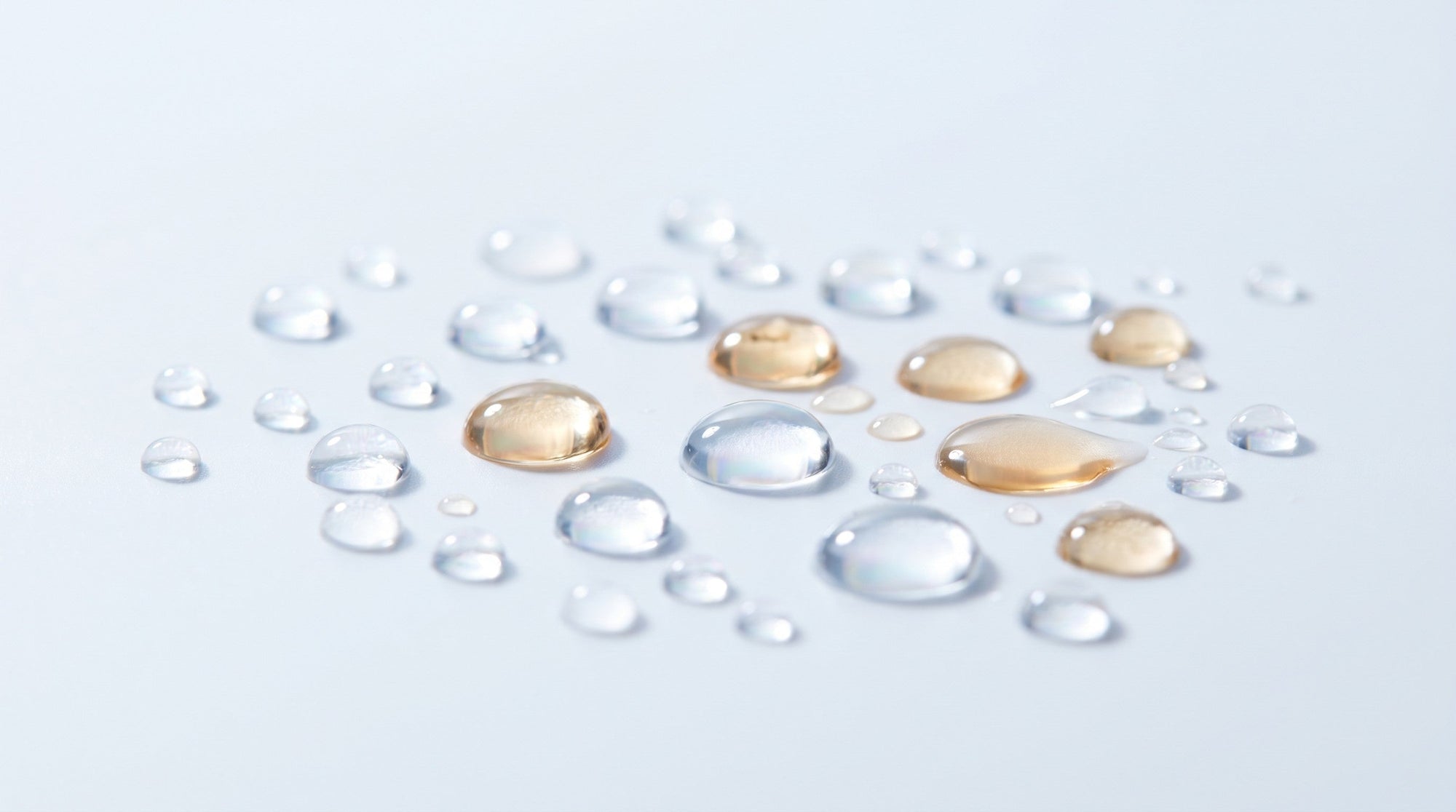 Macro of water and oil droplets beading and separating on a clean pale surface, light refracting through them.